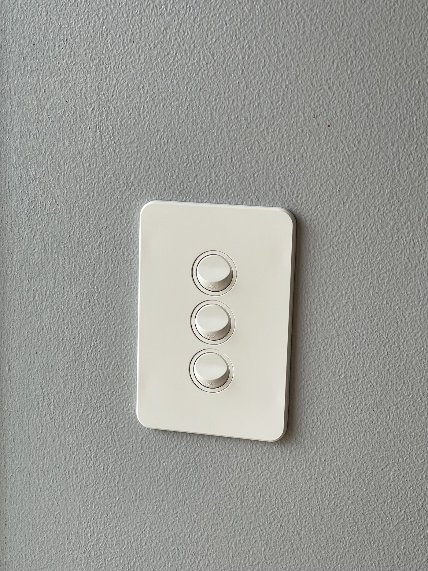 White three-button dimmer switch plate on a textured grey wall