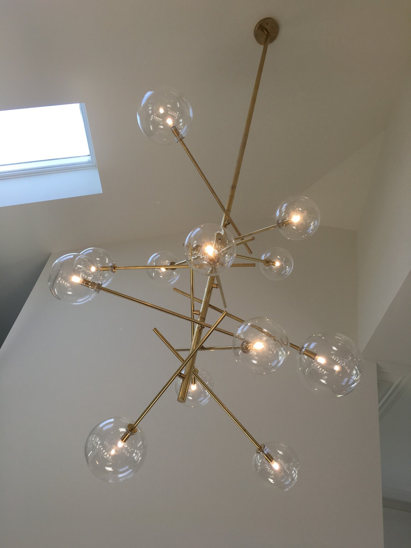 Brass multi-globe chandelier installed beneath a skylight in a high ceiling